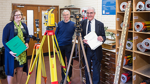 Three people stand with pieces of surveying equipment 